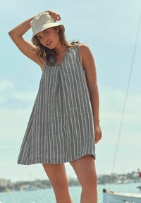 Vestido sin mangas a rayas gris y blanco con escote en V, hecho de tela ligera; combinado con un sombrero de cubo gris claro.