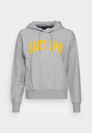 Sweat à capuche gris clair à manches longues avec le texte jaune « GANT 1949 » en lettres audacieuses et arquées sur la poitrine.