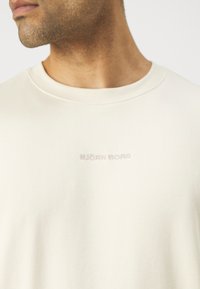 Cream-colored t-shirt with a round neckline, featuring subtle embossed "BJÖRN BORG" logo at the chest, made of soft fabric with a smooth texture.