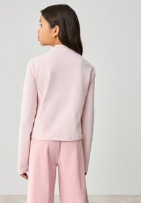 Světle růžový top s dlouhým rukávem, kulatým výstřihem a rovnými lemy. Měkká tkanina a minimalistický design v kombinaci s odpovídajícími růžovými kalhotami.