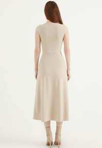 Beige, taillierte Midi-Kleid mit kurzen Kapellärmeln und einem ausgestellten Rock. Glatter Stoff und minimalistisches Design, kombiniert mit kniehohen Stiefeln mit Absatz.