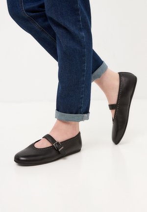 Zwarte leren Mary Jane flats met een bandje en gesp, met een ronde neus en studs langs de rand, gedragen met opgerolde denim.