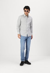 Világosszürke gombos ing, kis kék virágmintával, világoskék farmerral és fekete sportcipővel viselve; napszemüveg teszi teljessé az outfitedet.