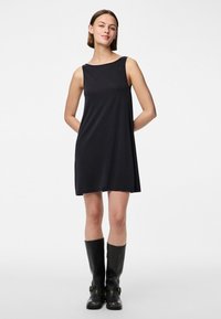 Μαύρο αμάνικο φόρεμα με χαλαρή εφαρμογή, λεία υφή και μήκος πάνω από το γόνατο, συνδυασμένο με μαύρες μπότες μέχρι το γόνατο που διαθέτουν πόρπες.