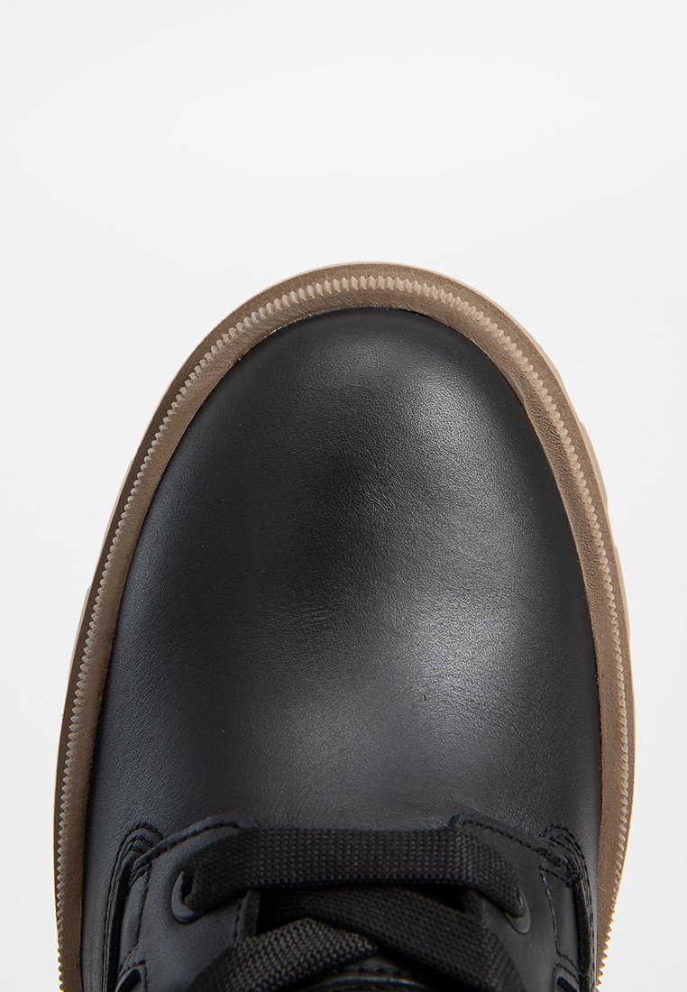 Scarpa in pelle nera con una finitura liscia, punta rotonda e suola in gomma marrone. Presenta lacci e cuciture neri lungo il bordo.