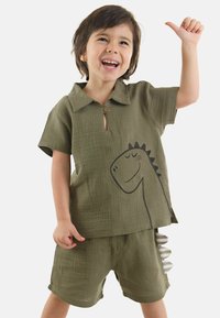 Olivgrön tvådelad outfit med texturerad tyg, som har en skjorta med krage och en dinosauries grafikkon samt shorts med accentdetaljer.