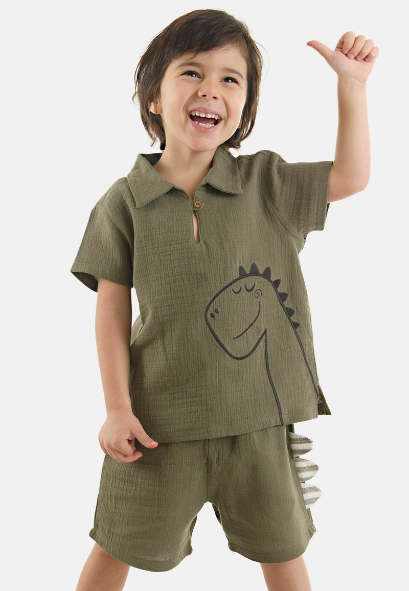 Olivgrön tvådelad outfit med texturerad tyg, som har en skjorta med krage och en dinosauries grafikkon samt shorts med accentdetaljer.