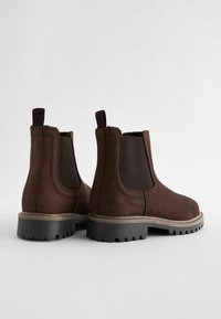 Bottines en cuir marron avec des panneaux latéraux élastiques, des coutures détaillées et des semelles en caoutchouc texturé.  orteils ronds et languettes à l'arrière.