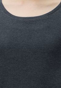 Gros plan d'une personne portant un t-shirt texturé gris foncé à col rond, montrant l'encolure et le haut de la poitrine.