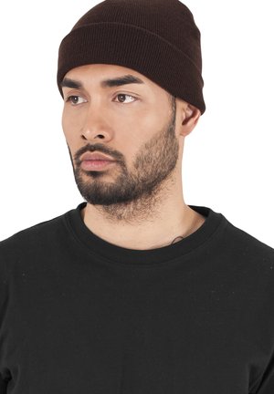Brown knit beanie with a ribbed texture, fitted snugly on the head. Worn with a black crew-neck sweatshirt. Clear facial features visible.