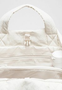 Zaino bianco trapuntato con doppio manico, tasca interna con zip, scomparto in rete e logo Lululemon. Presenta un tessuto morbido e una leggera trama.