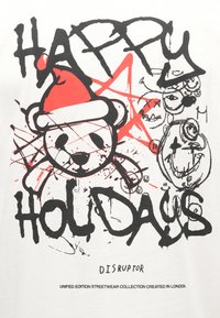 Hvid T-shirt med en bjørn iført en rød julemandshue, sort tekst i graffitistil med ordene "GLÆDELIGE HELLIGDAGE" og abstrakte drypmønstre.