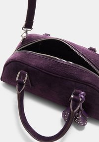 Lila Wildleder-Handtasche mit strukturiertem Finish, Reißverschluss, zwei Griffen und silberfarbener Hardware. Enthält dekorative Nieten an einem Charme.