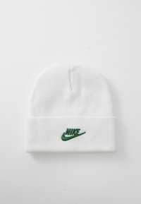 Balta megzta kepurė su užlenktu kraštu. Priekyje yra žalias išsiuvinėtas Nike logotipas. Minkšta tekstūra ir apvalus viršus.
