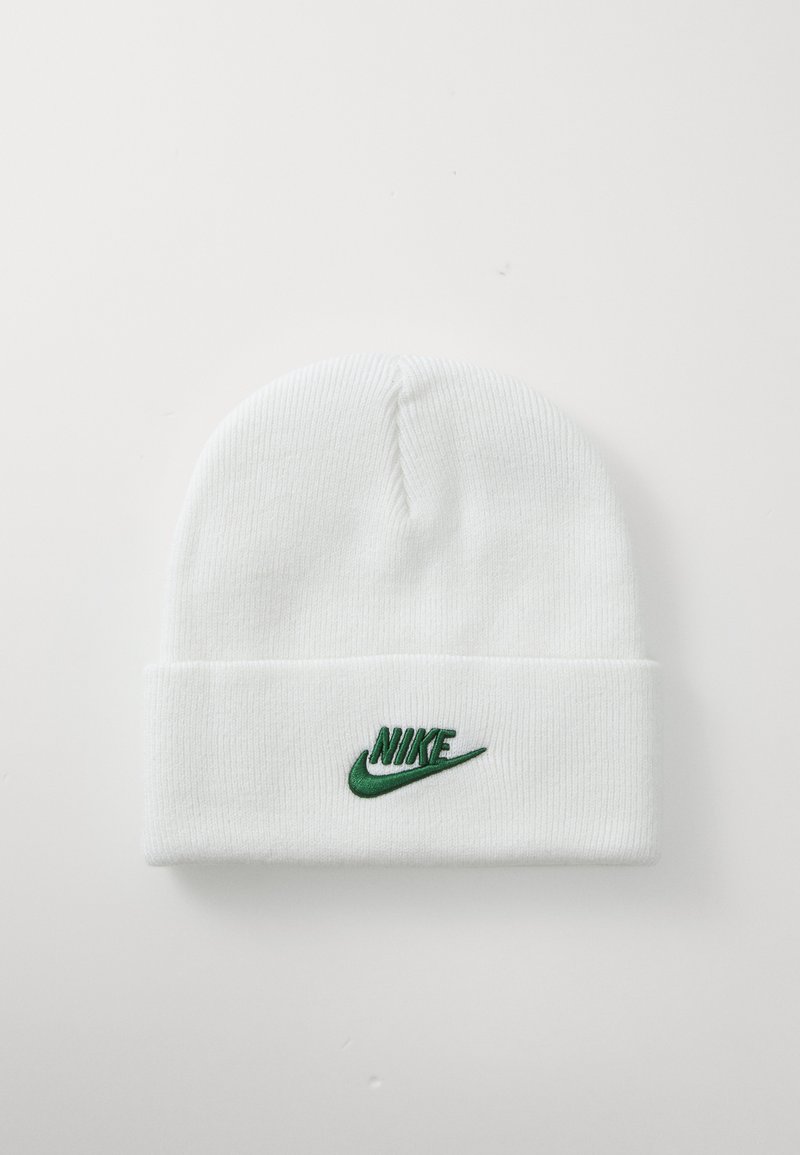 Balta megzta kepurė su užlenktu kraštu. Priekyje yra žalias išsiuvinėtas Nike logotipas. Minkšta tekstūra ir apvalus viršus.
