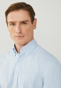 Camicia button-up azzurro chiaro con colletto classico, realizzata in un tessuto testurizzato. Presenta bottoni bianchi e una vestibilità sartoriale.