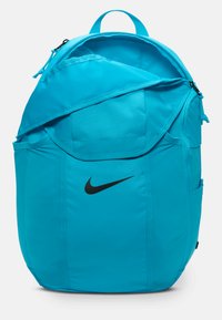 Teal ryggsekk laget av stoff, med et hovedrom med dobbel glidelås, sidelommer og en svart Nike-logo på fronten.