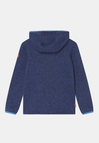 Tumedat merevoodid, millel on struktuurne kudumine, avara kapuutsi ja helesinised aktsendid varrukatel. Väike logo detail varrukal.