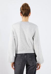 Felpa in cotone grigia con maniche lunghe e larghe e polsini a coste. Presenta un collo rotondo e una vestibilità cropped. Indossata con jeans scuri.