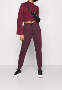 Top corto burdeos de manga larga y joggers a juego con cinturilla elástica. Combinado con un bolso cruzado negro y sneakers negros.