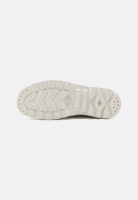 Suela de una zapato en goma blanco roto, con una superficie texturizada que presenta un patrón en zigzag, puntos de agarre circulares y surcos flexibles elevados.