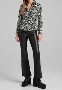 Black and white zebra-patterned shirt with a collar, paired with shiny black flared pants and chunky black platform boots.