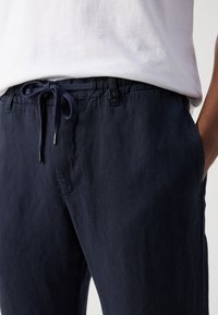 Navyblauwe linnenbroek met een elastische tailleband, een verstelbaar trekkoord en zijzakken. De stof heeft een casual, gestructureerde uitstraling.