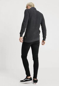 Tmavě šedý žebrovaný pletený svetr s vysokým límcem, úzkým střihem a dlouhými rukávy, doplněný černými úzkými džínami a černými teniskami.