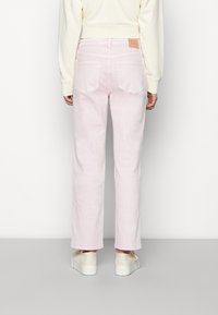 Jeans de ganga rosa claro com corte reto, cinco bolsos e um patch de couro castanho na parte de trás da cintura. Usados com ténis brancos.