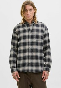 Camisa de franela con un patrón a cuadros en negro y gris, con botones en la parte delantera y un bolsillo en el pecho. Tejido suave con un corte holgado.