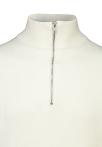 Ljus beige polotröja med halv dragkedja, ribbat mönster och mjukt material. Dragkedjan är silverfärgad och sluter sig vid halsen.