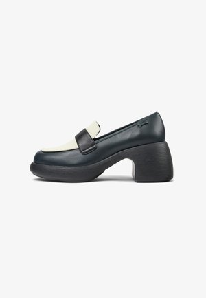Mocasín de cuero en verde azulado oscuro con un acento crema en la punta, que presenta un tacón chunky de madera negra y una textura suave.