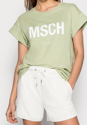 Hellgrünes T-Shirt mit weißem "MSCH"-Aufdruck, rundem Ausschnitt und hochgekrempelten Ärmeln, kombiniert mit weißen Shorts mit Kordelzug. Glatte Textur.