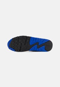 Čierna gumová podrážka s modrými akcentmi, textúrovaný gripový vzor a vlnitý dizajn. Logo Nike viditeľné v oblasti pätky.