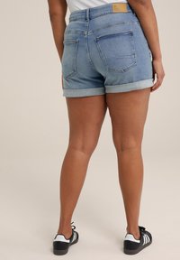 Ljust blå denimshorts med uppvikta fållar, med två bakfickor och en brun etikett vid midjan. Matchas med svarta sneakers.