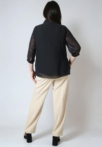 Zwarte doorzichtige blouse met 3/4 mouwen, losse pasvorm, gecombineerd met beige wijde broek. Toont een gladde textuur en een eenvoudig ontwerp.