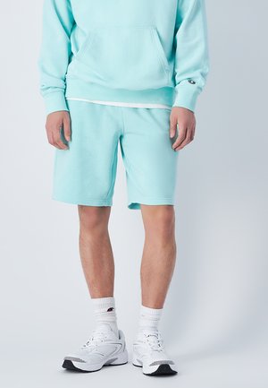 Sudadera de algodón azul claro con un bolsillo frontal y pantalones cortos a juego. Presenta un corte relajado y acentos blancos en los calcetines y el calzado.