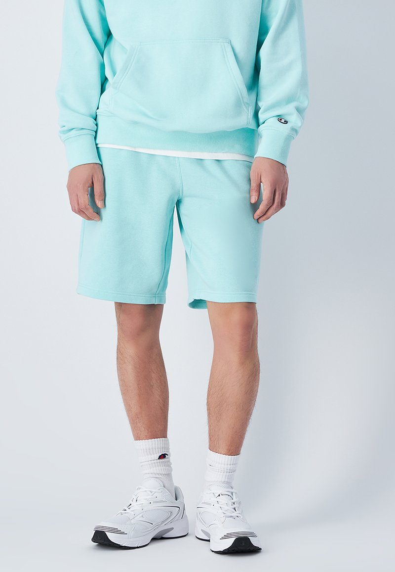 Sudadera de algodón azul claro con un bolsillo frontal y pantalones cortos a juego. Presenta un corte relajado y acentos blancos en los calcetines y el calzado.