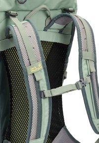 Gros plan sur les bretelles vertes d'un sac à dos de randonnée Jack Wolfskin, avec un rembourrage en mesh, une boucle de poitrine réglable et une poignée de transport.