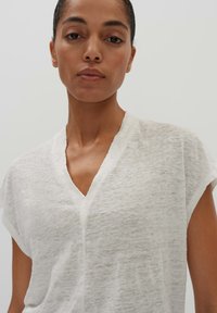 Top bianco a maniche corte con scollatura a V e tessuto morbido e testurizzato. Il design è a vestibilità rilassata con dettagli di cucitura discreti.