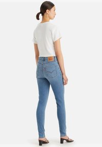 Vaqueros skinny de mezclilla azul con cintura alta, con bolsillos traseros y una etiqueta de cuero marrón. Combinados con una camiseta blanca sencilla.