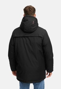 Giacca isolante nera con cappuccio, caratterizzata da una texture liscia, polsini elasticizzati e una leggera lucentezza. Include un dettaglio con logo sul retro.