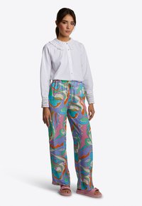 Witte blouse met kantkraag, gecombineerd met kleurrijke wijduitlopende broek in roze, groen en blauw. Roze slippertjes.