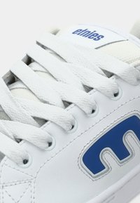 Λευκό αθλητικό παπούτσι με υφή από δερματίνη, μπλε λογότυπο και λευκές επίπεδες κορδόνες. Διαθέτει έξι τρύπες κορδονιών και επενδυμένη γλωττίδα για άνεση.