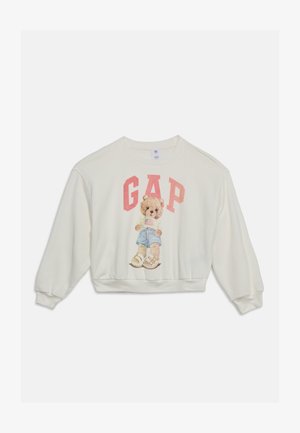 Witte trui met een teddybeer die korte broek en sandalen draagt, een Amerikaanse vlag vasthoudend, met grote roze "GAP"-tekst erboven.