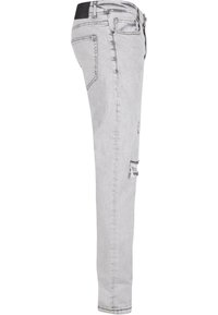 Jean skinny en denim gris clair avec des détails usés, cinq poches et une taille noire. Présente une texture lisse et un design ajusté.