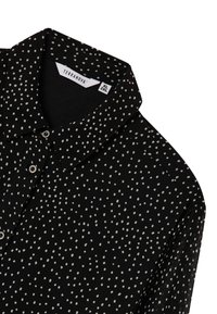 Blusa nera con pois bianchi, dotata di colletto classico e chiusura a bottoni. Tessuto morbido con una consistenza liscia. Etichetta del brand visibile.