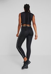 Czarny sportowy crop top z okrągłym dekoltem, w zestawie z czarnymi legginsami o wysokim stanie z białymi bocznymi paskami i akcentami logo.