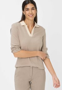 Gestreiftes Poloshirt in Beige und Hellbraun mit einem kontrastierenden Kragen. Die langen Ärmel sind hochgekrempelt, und der Stoff hat eine strukturierte Oberfläche.