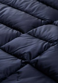 Námornícky modrý prešívaný materiál s jemným leskom, ktorý sa vyznačuje veľkými, polstrovanými sekciami a hladkou textúrou, navrhnutý pre teplo a pohodlie.